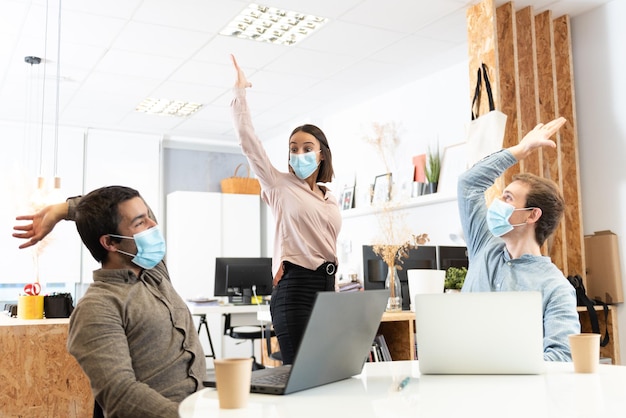 Happy coworkers celebrating with the hands up while wearing protective masks