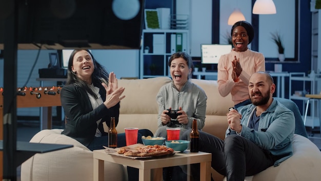 Happy coworkers playing video games after work at office.\
colleagues enjoying win using controllers on television console to\
do fun activity with entertainment. workmates winning game