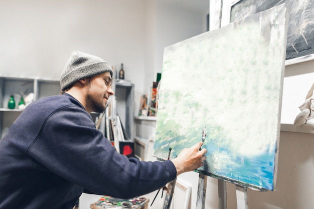 Happy creative artist sits on the chair at the studio and works on the picture