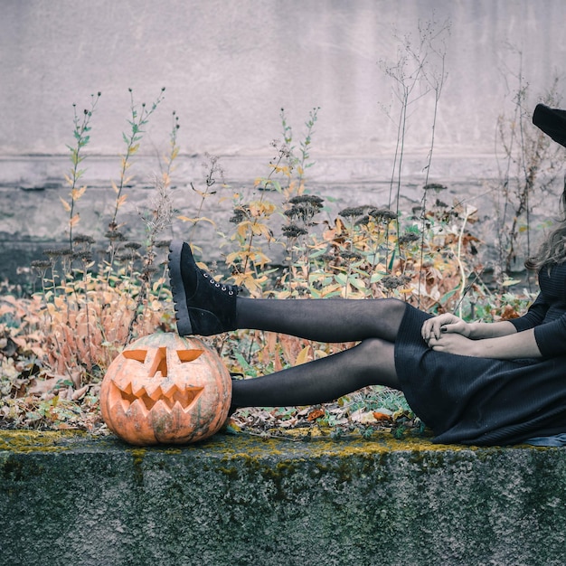 Foto felice raccapricciante giovane donna gotica irriconoscibile in costume da strega di halloween con la zucca di halloween