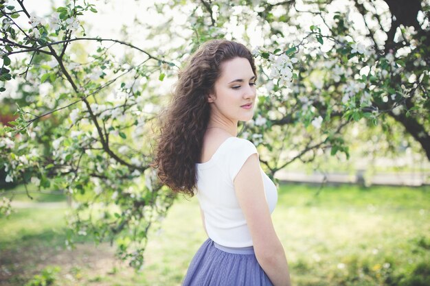 Happy curly hair young woman in a white t-shirt under the blooming apple tree