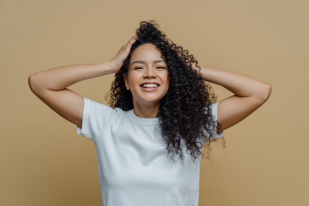 Happy curly woman keeps hands on head