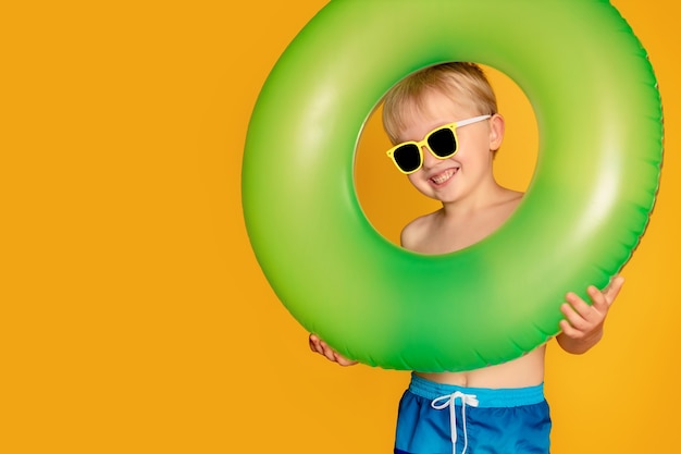 Happy cute baby boy 6-7 years old in sunglasses and with a life buoy. Summer and the sea.