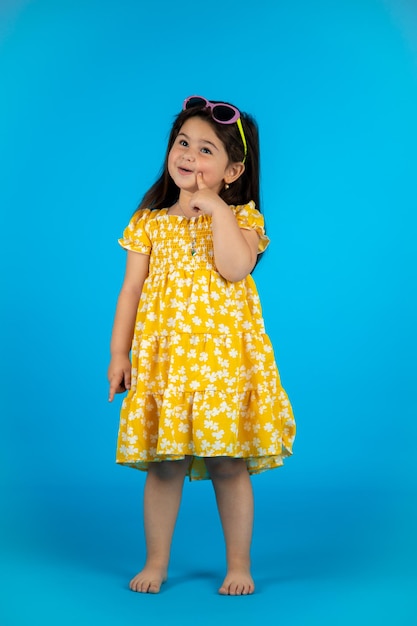 Happy cute baby girl fashionable yellow baby clothes posing studio on blue background