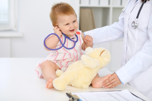 Happy cute baby at health exam at doctor's office Toddler girl is sitting and keeping stethoscope and teddy bear