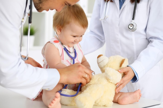 Foto bambino carino felice all'esame di salute presso l'ufficio del medico la ragazza del bambino è seduta e tiene uno stetoscopio e un orsacchiotto