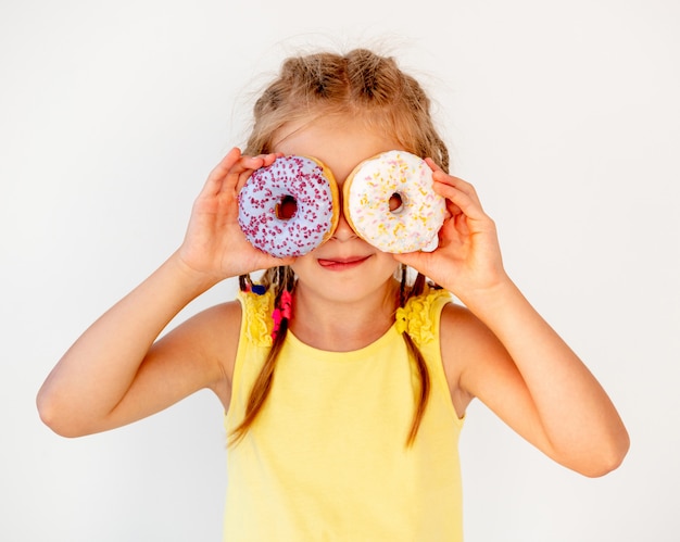 Happy cute blond girl holding two donuts on her eyes