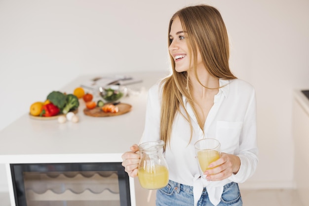 幸せなかわいい金髪の女性がキッチンでオレンジ ジュースを飲む