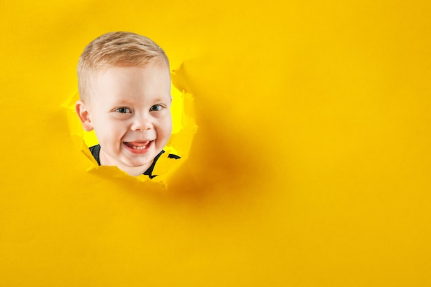 Happy cute boy climbs through a hole in the paper. Bright photo of a boy.