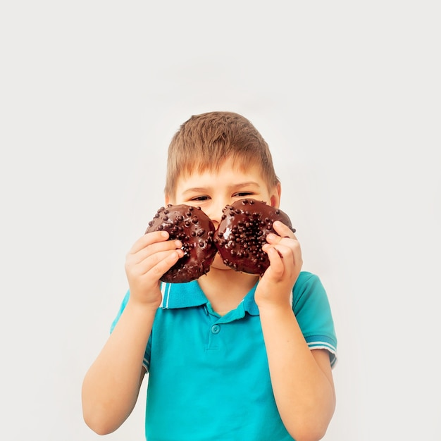 Happy cute boy has fun playing with donuts on a light wall. Chocolate donuts