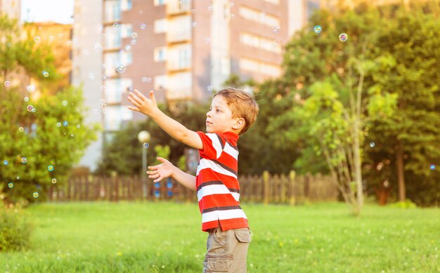 Happy cute boy playing to catch soap bubbles in the park