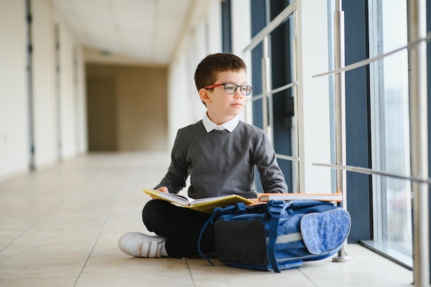 Happy cute clever boy in glasses with school bag and book in his hand First time to school Back to school