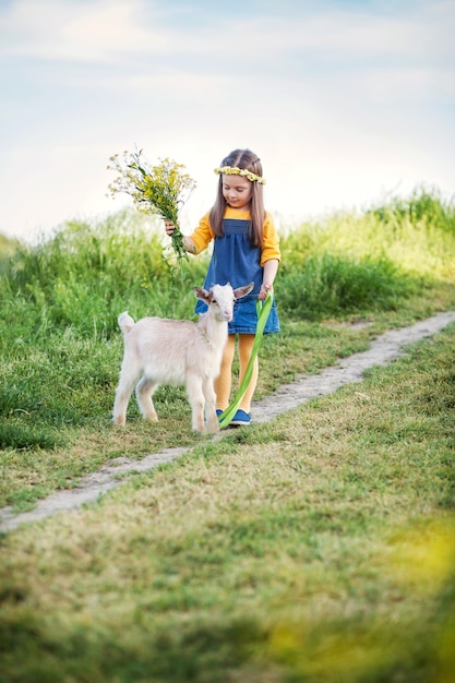счастливая милая девочка 4-5 лет на прогулке с козой в поле