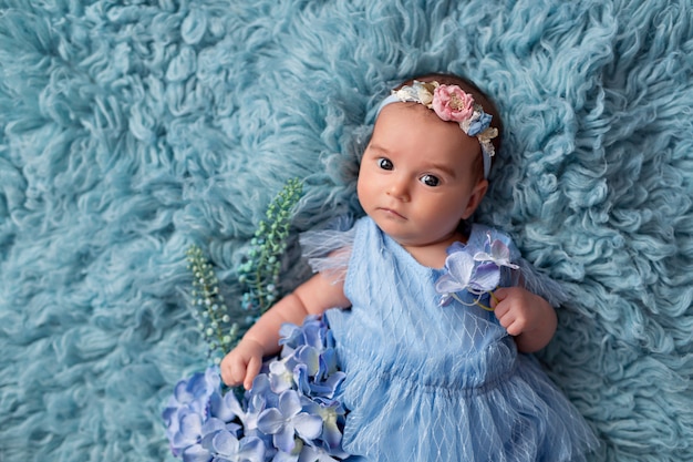 Happy cute girl in a blue dress lies on her back with flowers.