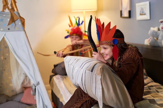 Happy cute girl in headdress of native americans shooting from bow