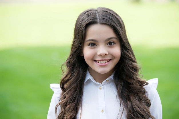 Happy cute kid smile in school uniform wearing long wavy brunette hair outdoors, haircare.