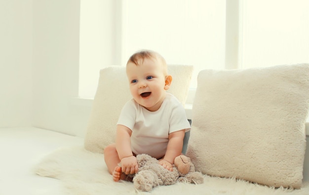 Happy cute little baby playing with teddy bear toy in white room at home