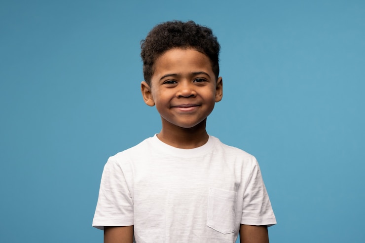 Photo happy cute little boy of african ethnicity in white t-shirt standing in front of camera against blue