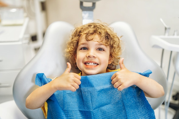 Happy cute little boy in dental ofiice showing thumbs up after treatment.