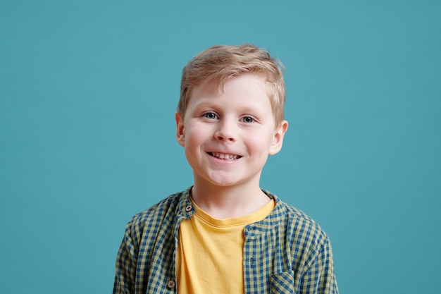 Happy cute little boy looking at you on blue background