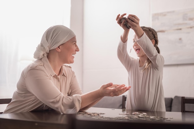 Happy cute little child with sick grandmother in kerchief playing with jigsaw puzzle together