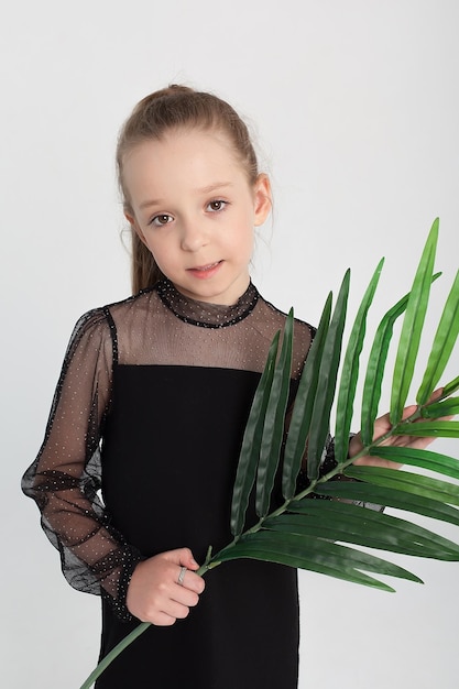 A happy cute little girl of 7 years old in a black dress smiles and looks at the camera studio portrait