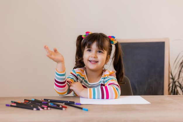 A happy cute little girl in a drawing lesson raises her hand at the top high quality photo