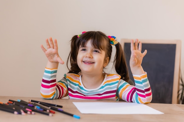 A happy cute little girl in a drawing lesson raises her hand at the top