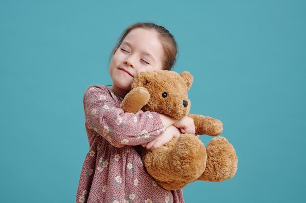 Счастливая милая маленькая девочка, обнимая своего пушистого коричневого медвежонка
