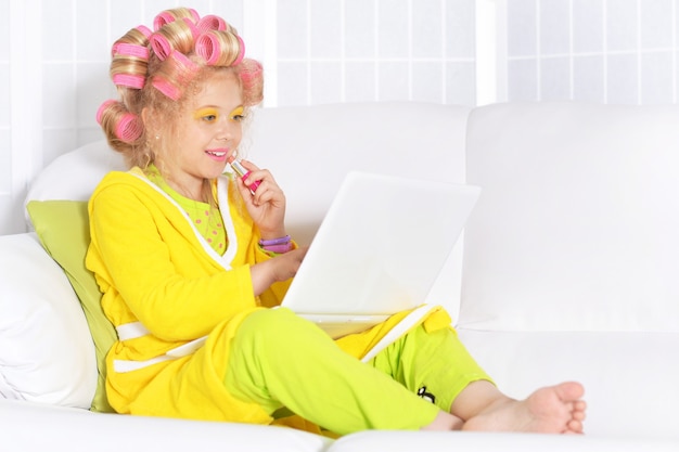 Happy cute little girl in hair curlers and laptop