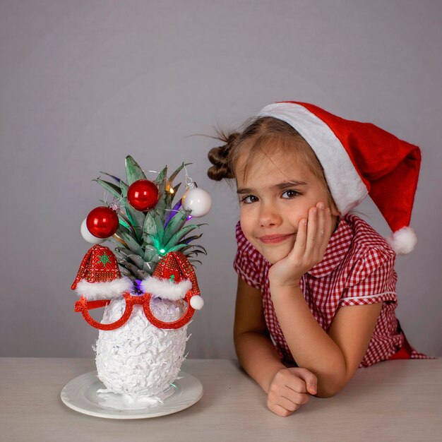 Felice bambina carina vicino al volto di babbo natale fatto con ananas