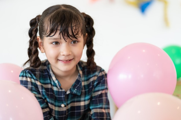 小学校のパーティーでピンクの風船を持って座っている幸せなかわいい女の子