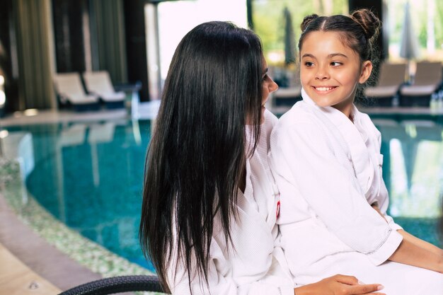 Happy cute little girl with her mother in bathrobes are joyful together while sitting in the spa salon