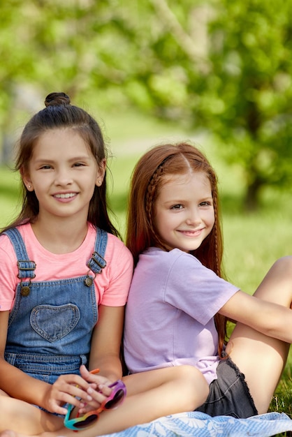 Bambine sveglie felici che si siedono insieme nel parco. amicizia e infanzia