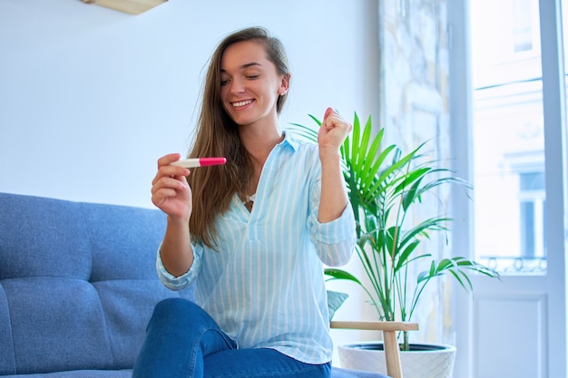 幸せなかわいい満足している若い笑顔の女性は、陽性の妊娠検査結果で喜ぶ