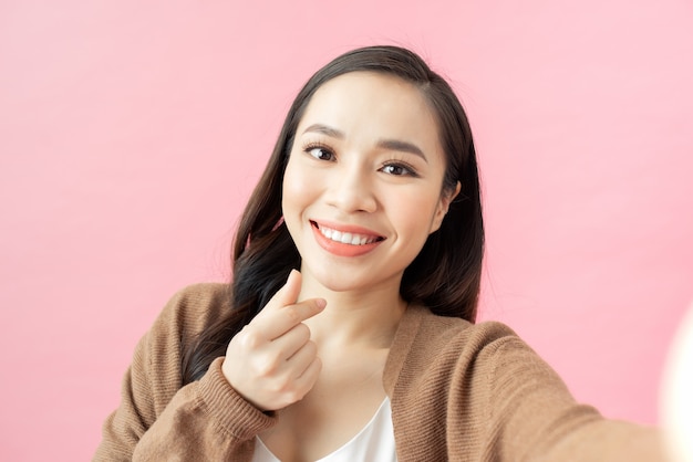 Happy cute woman making selfie over pink background.