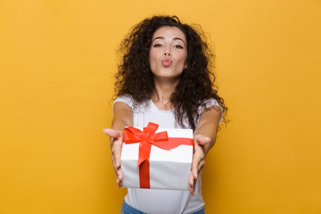 Happy cute young woman posing isolated on yellow holding gift box present