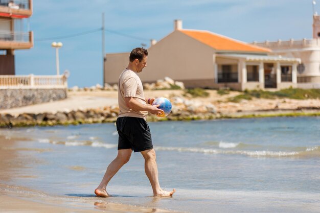 Happy dad adult man on the beach plays with a ball on the sand Travel and leisure