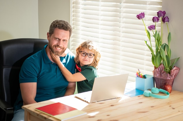 Happy dad helping his school son child in glasses study with computer at home education