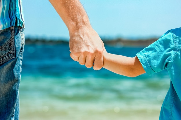 A happy dad holds the hand of a child by the greek sea in nature