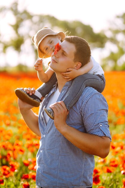 Happy dad and little baby girl having fun in field of flowering poppie kisses of father and daughter