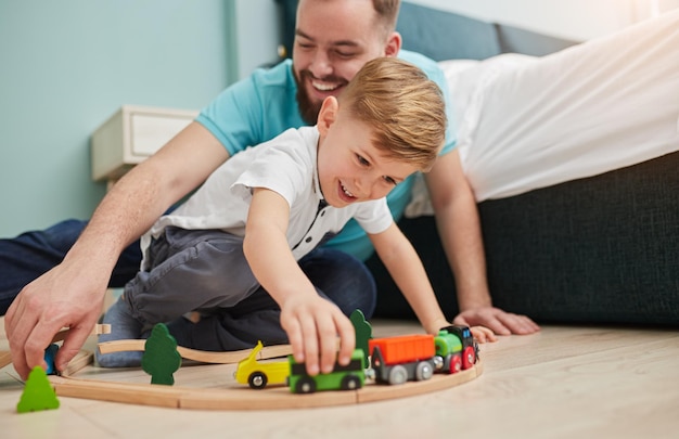 Happy dad and little boy playing toy train on floor while spending free time together at home