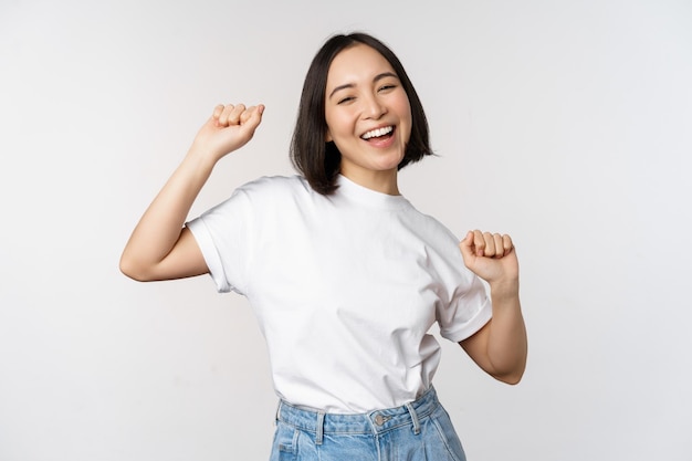 Tシャツを着て白い背景に対してポーズをとって幸せなダンス韓国の女の子