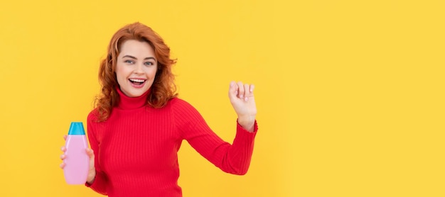 Felice danza rossa donna capelli ricci tinti che presenta il prodotto per la cura del corpo del trattamento dei capelli con shampoo