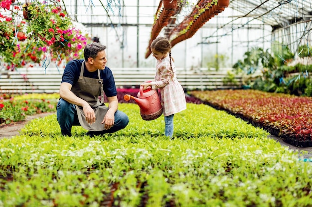 Happy daughter assisting her father in a plant nursery and watering flowers with a watering can