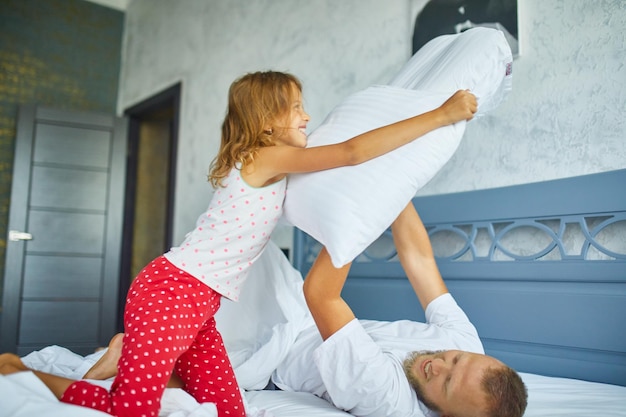 Happy daughter and father playing pillow fight in bed at morning at home, fighting with pillows, have fun play together at home on family weekend