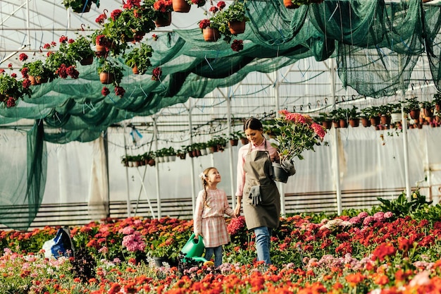 Happy daughter holding hands with mother while walking through greenhouse and taking care of flowers