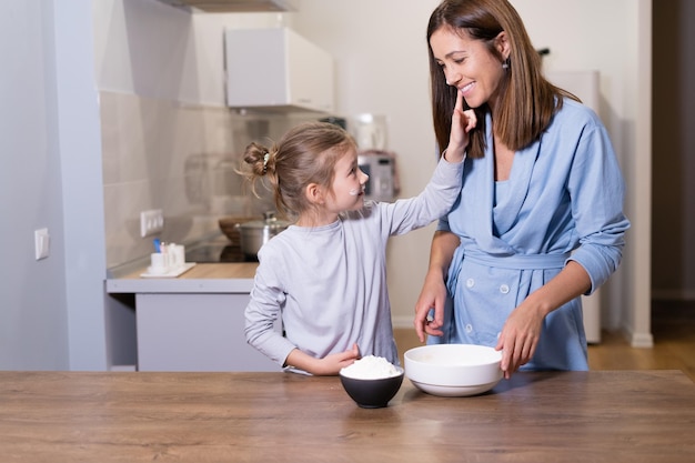 Happy daughter laughs with her mother while kneading dough in the modern kitchen at Sweet Home Smiling family preparing delicious cookies