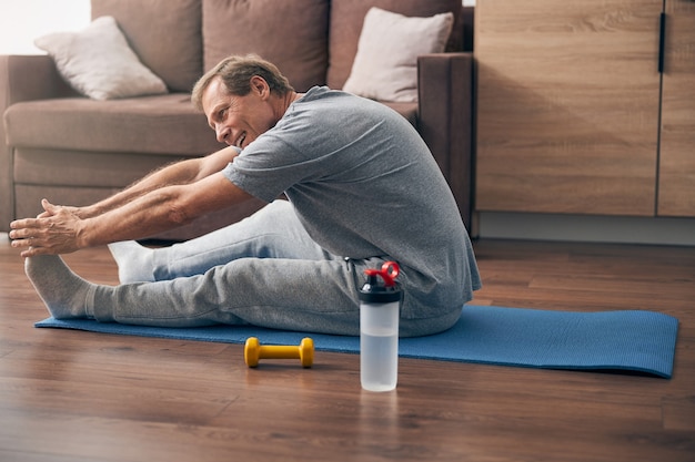 Happy delighted adult man keeping smile on his face while doing sport at home