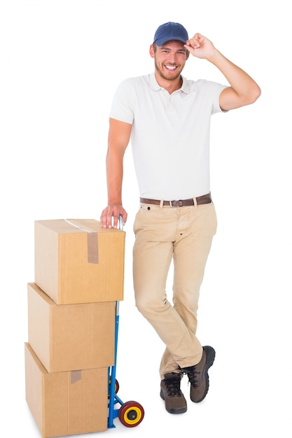 Happy delivery man leaning on trolley of boxes